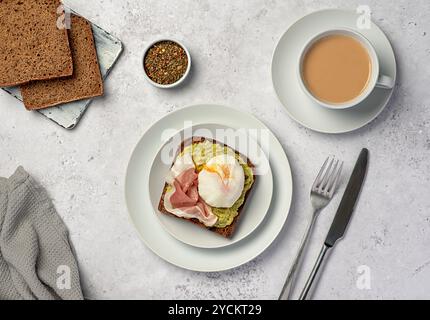 Fotografia gastronomica della colazione nutrizionale, pane di segale a pasta madre con purè di avocado, prosciutto, pancetta, uovo bollito, tè con latte Foto Stock