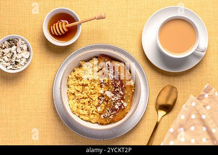 Fotografia gastronomica di porridge di miglio con banana caramellata, noci pecan, noci, fiocchi di cocco, chia, semi di lino, miele, tè con latte di mandorle Foto Stock