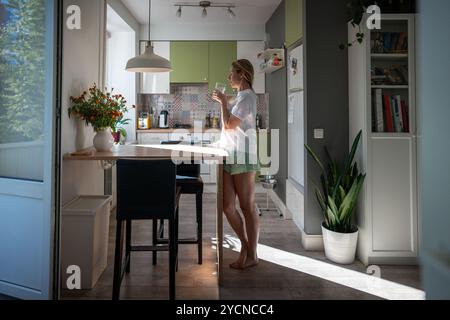 Donna che beve acqua fresca in cucina, inizia la giornata con un tocco rinfrescante. Equilibrio dietetico, mattina energizzante Foto Stock