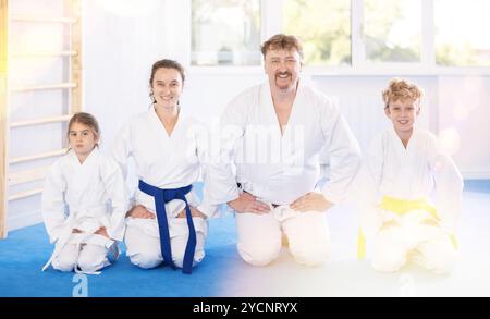 Genitori sorridenti con bambini preadolescenti in kimono seduti in ginocchio su tatami Foto Stock