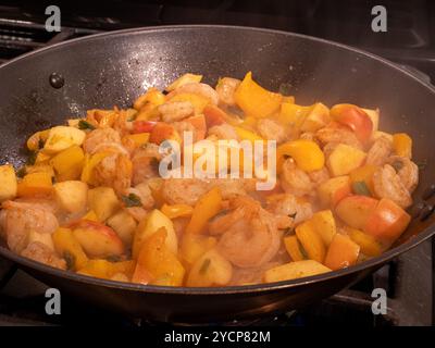 Un piatto vivace e salutare con gamberi, mele e peperoni gialli spolverati con curry in polvere in una padella di ferro con vapore dal caldo, che offre un colon Foto Stock