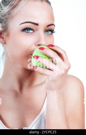 La giovane donna bionda ha gioiosamente in mano una vivace mela verde, pronta a prendere un morso croccante, che irradia felicità e salute Foto Stock