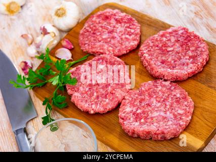 Polpette di manzo crude per hamburger su tavola di legno con spezie Foto Stock