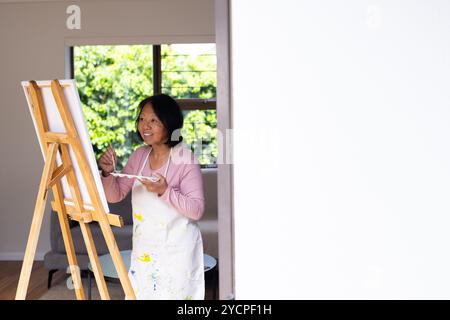 donna asiatica anziana che dipinge su tela a casa, godendo della solitudine creativa Foto Stock