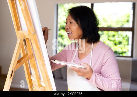 Anziana donna asiatica anziana che dipinge su tela a casa, godendo della solitudine creativa Foto Stock