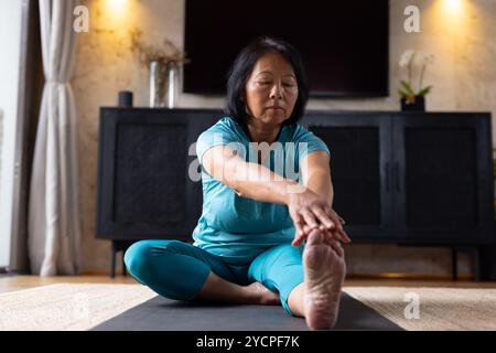 Donna asiatica anziana che pratica yoga a casa, si allunga sul tappeto con attenzione Foto Stock