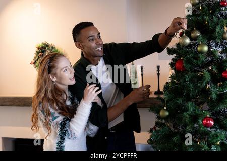 Coppia multirazziale che decora l'albero di Natale a casa, godendo dello spirito festivo Foto Stock