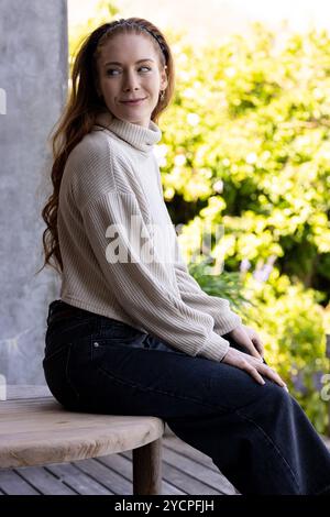 Donna sorridente seduta su una panchina di legno all'aperto, godendosi una giornata di sole Foto Stock