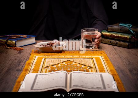 Molte palme di datteri sono su ciotole, piatti e tazze d'acqua, e il Corano è su tavoli di legno, per aspettare il tempo di Iftar, con il concetto di ramadan Foto Stock