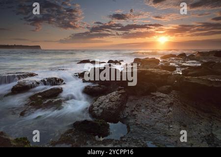 L'alba sulla spiaggia di Warriewood con la bassa marea, con i suoi dolci flussi e le graziose nuvole altocumulus oscurano parzialmente il sole, i suoi caldi raggi invernali evidenziano il wa Foto Stock