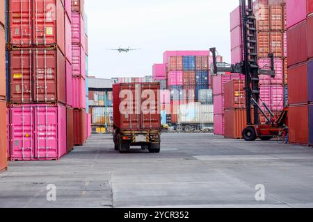 Un deposito di container e carrelli elevatori funzionano sotto un cielo parzialmente nuvoloso. Foto Stock