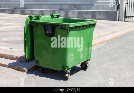 Aperto di plastica verde contenitore di riciclaggio presso la soleggiata città street Foto Stock