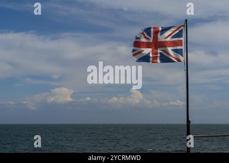 Una bandiera di Union Jack strappata e lacerata in un vento rigido con oceano blu e cielo dietro Foto Stock