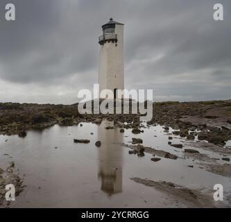 Una vista dello storico Southerness Lighthouse in Scozia con riflessi nelle piscine di marea in primo piano Foto Stock