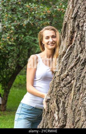 Primo piano, giovane donna amante della natura che abbraccia un albero enorme Foto Stock