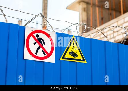 Segnali di avvertenza e filo spinato sulla recinzione del cantiere Foto Stock