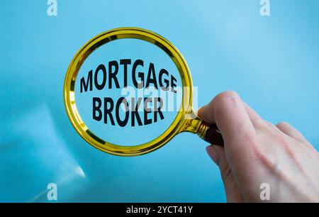 Simbolo del broker ipotecario. Lente d'ingrandimento con parola concettuale Mortgage Broker. Mano d'affari. Bellissimo sfondo blu. Intermediario finanziario e ipotecario Foto Stock