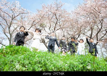 I nuovi studenti del primo anno si tengono per mano in una fila di alberi di ciliegio in fiore Foto Stock