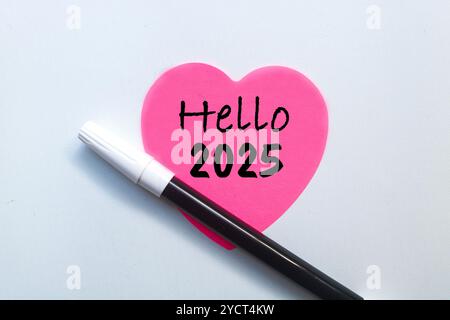 Nota adesiva d'amore rosa con scritto Hello 2025 su di essa con penna isolata su sfondo bianco. Diamo il benvenuto al nuovo concetto del 2025 Foto Stock