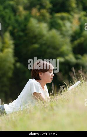 Donna sdraiata nella prateria a leggere un libro Foto Stock