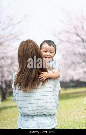 Madre che tiene un bambino dietro sul viale alberato di ciliegi Foto Stock