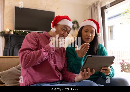 Coppia senior multirazziale in video chat con Babbo Natale su tablet, godendosi il Natale a casa Foto Stock