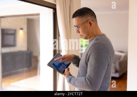 Uomo anziano asiatico che usa il tablet per controllare il sistema di casa intelligente per finestra Foto Stock