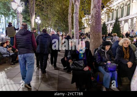 Tbilisi, Georgia. 23 ottobre 2024. Le persone si rilassano sulle panchine e altri camminano lungo una strada alberata a Tbilisi mentre partecipano a una pacifica manifestazione pre-elettorale. Gli alberi e le luci della strada creano un'atmosfera intima ma energizzata. Catturato durante la campagna pre-elettorale a Tbilisi, Georgia, mercoledì 23 ottobre 2024. (VX Photo/ Vudi Xhymshiti) crediti: VX Pictures/Alamy Live News Foto Stock