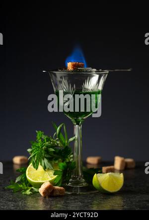 Bruciare lo zucchero su un bicchiere con assenzio. Preparazione della bevanda. Absinthe con ingredienti su sfondo nero. Foto Stock