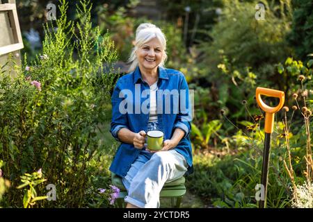 Donna anziana che si rilassa nel suo giardino con una tazza di tè in mano Foto Stock