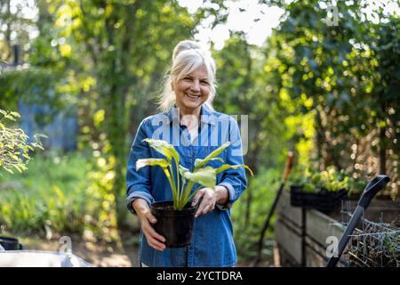 Ritratto di una donna anziana sorridente che tiene una pianta in vaso nel suo giardino Foto Stock