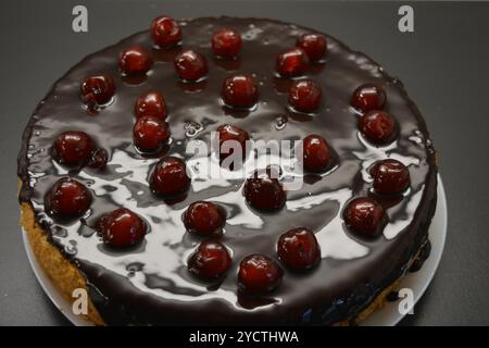 Torte fatte con le tue mani. Torta bianca in spugna "ciliegia secca" decorata con glassa di cioccolato con ciliegie dolci caramellate, rosse e brillanti. Foto Stock