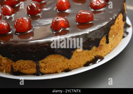 Torte fatte con le tue mani. Torta bianca in spugna "ciliegia secca" decorata con glassa di cioccolato con ciliegie dolci caramellate, rosse e brillanti. Foto Stock