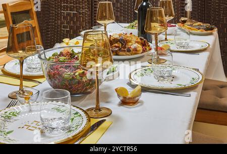 Un tavolo da pranzo elegantemente allestito per un pasto festivo, con bicchieri da vino, piatti e un vibrante pezzo centrale per insalate. Iscrizione ebraica: Buona y Foto Stock