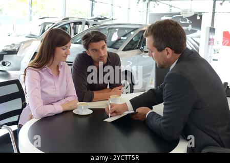 Coppia giovane l'acquisto di una nuova auto nello showroom di una concessionaria auto - firma del contratto di vendita con il venditore Foto Stock