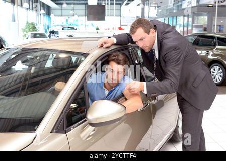 Consulenza in concessionaria auto - venditore e giovane uomo che vende una nuova auto Foto Stock