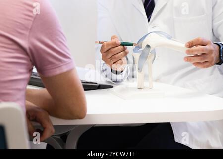 Medico che mostra legamenti del ginocchio su un modello a un paziente durante una consultazione, incentrato sull'anatomia e sulla salute articolare Foto Stock