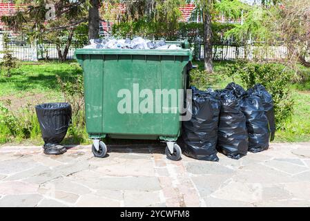 Aperto di plastica verde contenitore di riciclaggio dei rifiuti e la plastica sacchi della spazzatura presso la soleggiata città street Foto Stock