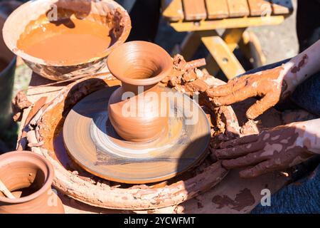 Le mani di un vasaio, creazione di un vasetto di ceramica sul cerchio. Lavorare sul tornio del vasaio all'aperto Foto Stock