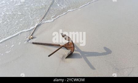 Ancora sulla sabbia, ancora arrugginita legata alla barca in mare, costa e ancora arrugginita Foto Stock