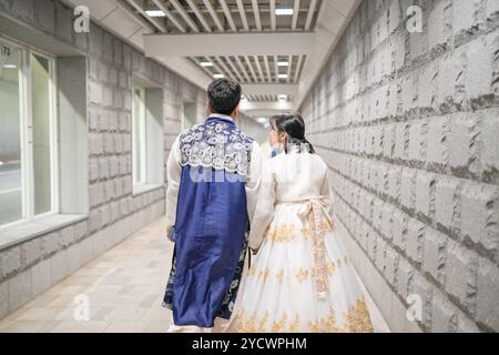 Uomo e donna stanno camminando lungo un corridoio. L'uomo indossa una giacca blu e la donna indossa un vestito bianco Foto Stock