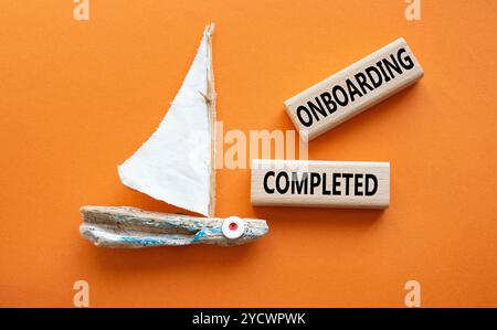 Simbolo onboarding completato. Termine concettuale onboarding completato su blocchi di legno. Bellissimo sfondo arancione con barca. Business and Onboarding Comple Foto Stock