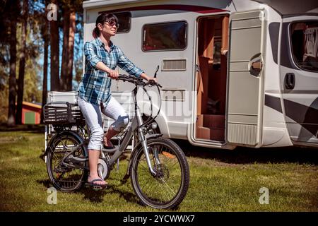 Donna sulla bicicletta elettrica in appoggio al campeggio. Vacanza per la famiglia in viaggio, viaggio vacanza in camper, caravan auto vacanza. Foto Stock