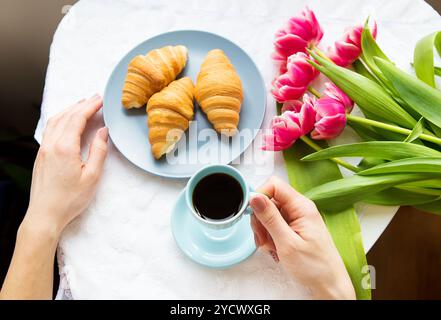 Ragazza con croissant e caffè, un bouquet di tulipani rosa, mattina felice. Foto Stock