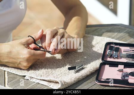 Una donna che fa la sua manicure. La ragazza si siede su un tavolo di legno, stende un set per manicure e un asciugamano, e rifinisce le gambe con forbici, primo piano Foto Stock