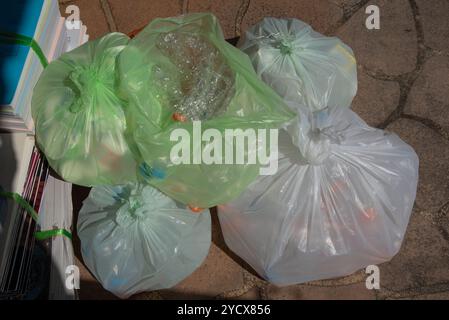 Vista dall'alto di diversi sacchetti di plastica legati riempiti di articoli riciclabili, inclusi i flaconi di plastica, posizionati su un pavimento esterno. Foto Stock