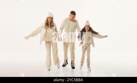 La famiglia ama passare il tempo sulla pista di pattinaggio, sorridendo e tenendosi per mano, catturando la gioia di passare del tempo insieme durante la stagione invernale contro il bianco Foto Stock