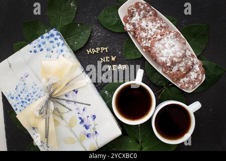 Iscrizione del nuovo anno su una lavagna nera con regalo, muffin e caffè. Foto Stock