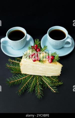 Fetta di torta decorata con alberi e frutti di bosco su sfondo nero con due tazze di caffè Foto Stock