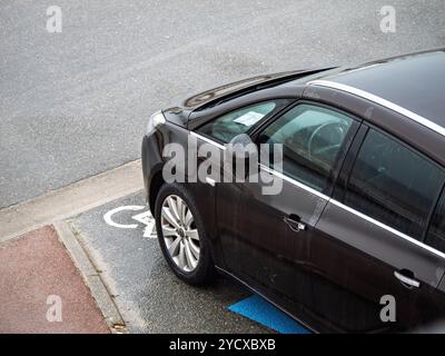 Neufchatel-Hardelot, Francia - 18 agosto 2023: Un'auto OPEL nera è parcheggiata in un parcheggio per disabili designato; contrassegnata dal simbolo della sedia a rotelle sul terreno bagnato; sottolinea l'accessibilità. Foto Stock